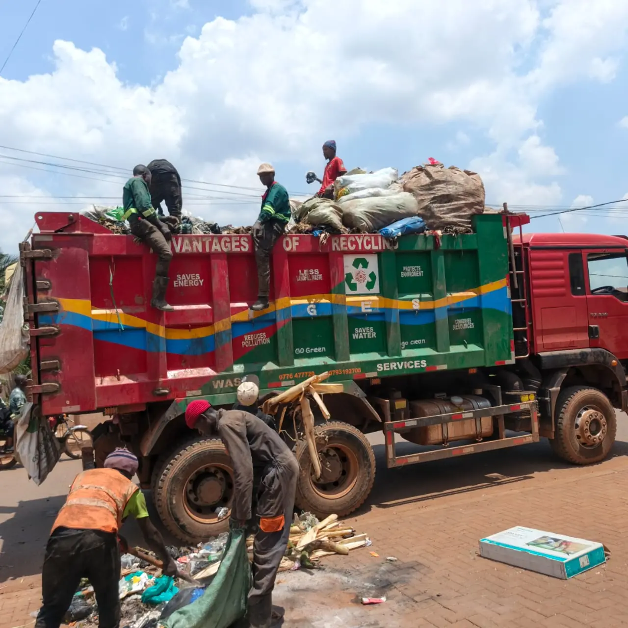 IGES crew in orange vests loading roadside waste into a red and green tipper truck