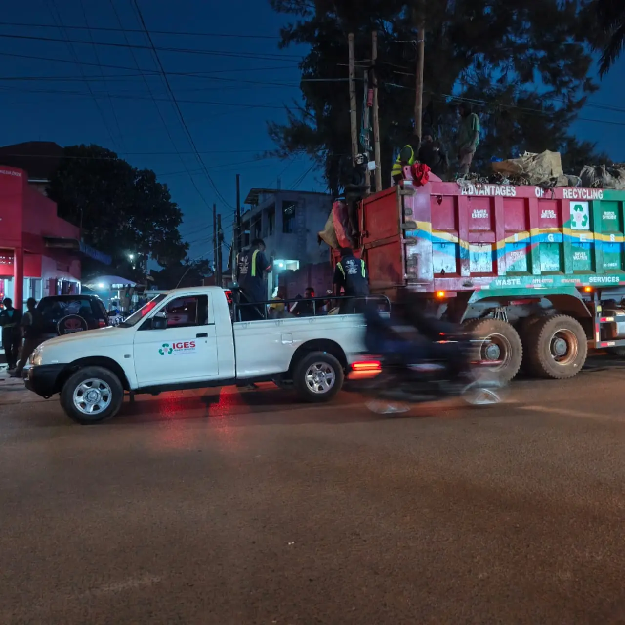 A white IGES pickup and a loaded tipper on a street at dusk