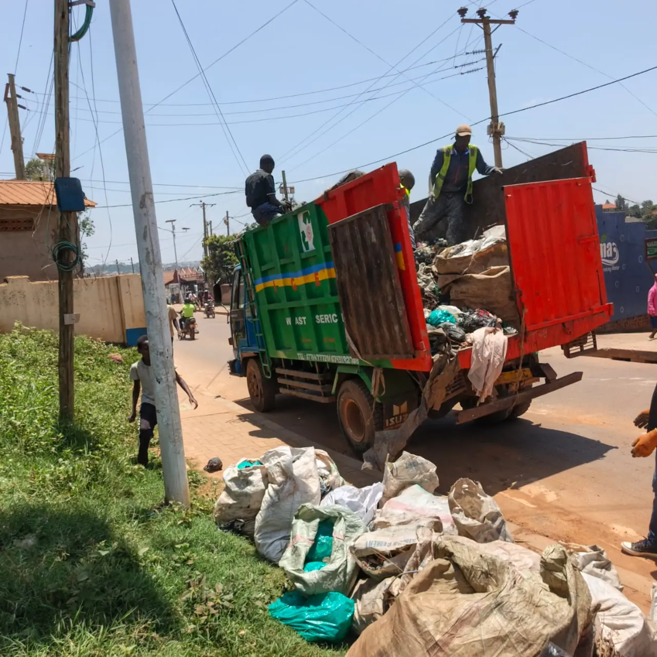 Crew loading sacks of waste into a green and red tipper at the roadside