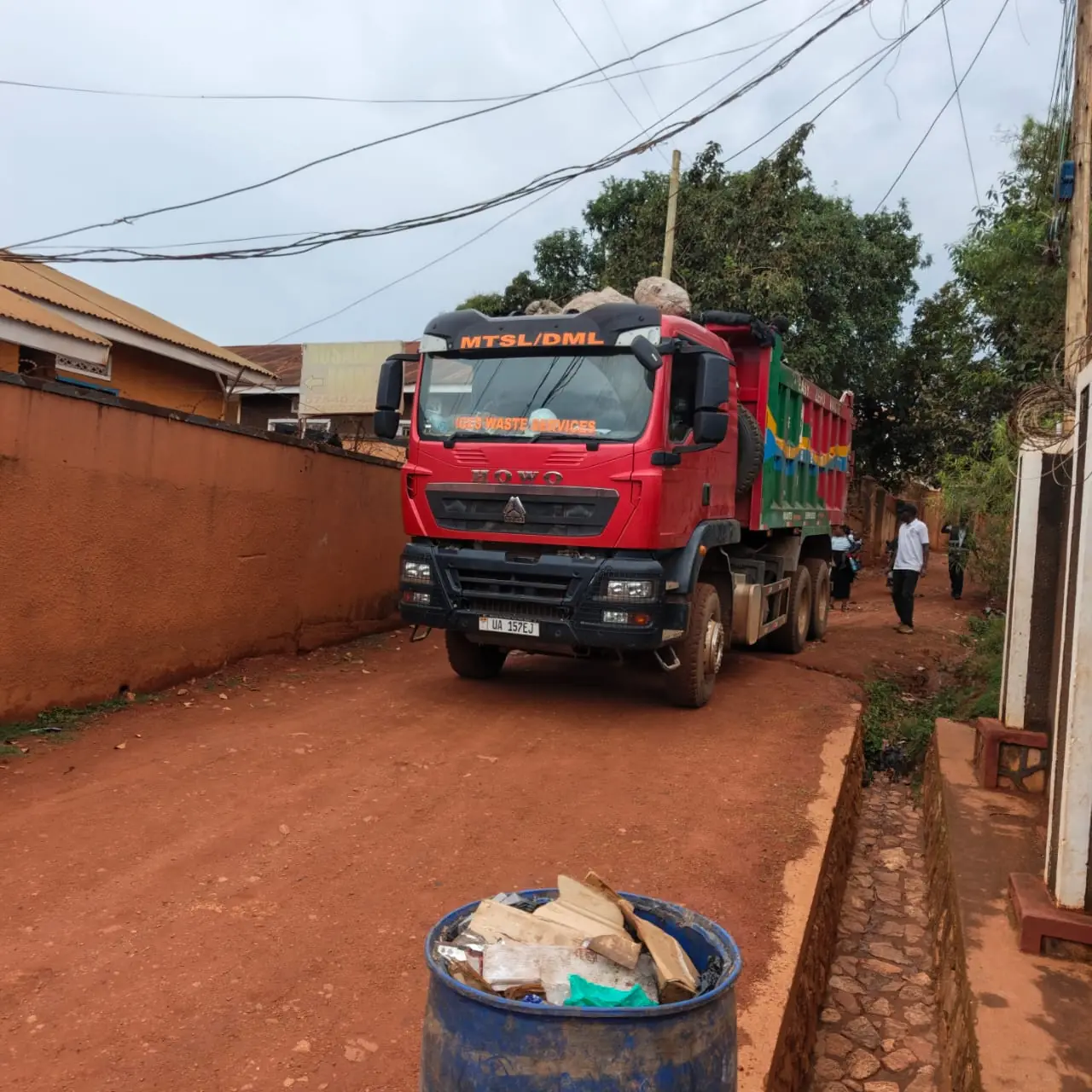 The HOWO tipper coming down a red-earth lane towards a full blue bin